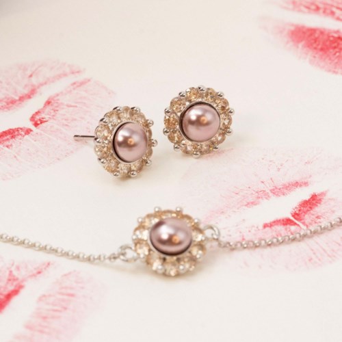 Elegant sieradenset met roze parels en omringende heldere stenen, omvat oorbellen en ketting, op een witte en roze achtergrond.