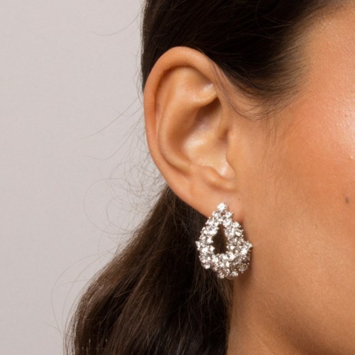 A woman wears a teardrop-shaped, sparkling diamond earring on her ear.
