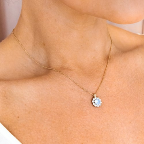 Een vrouw draagt een fijne gouden ketting met een lichtblauwe edelsteen hanger omgeven door kleinere stenen.