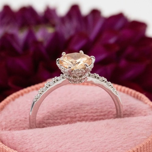 En sølvring med en stor oval ædelsten omgivet af små diamanter, vist på en pink velvetskrin.