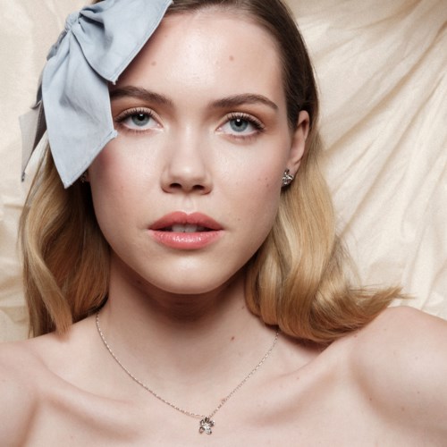 A woman with light brown hair, blue eyes, wearing a gray headband and a necklace, resting on a light-colored pillow.