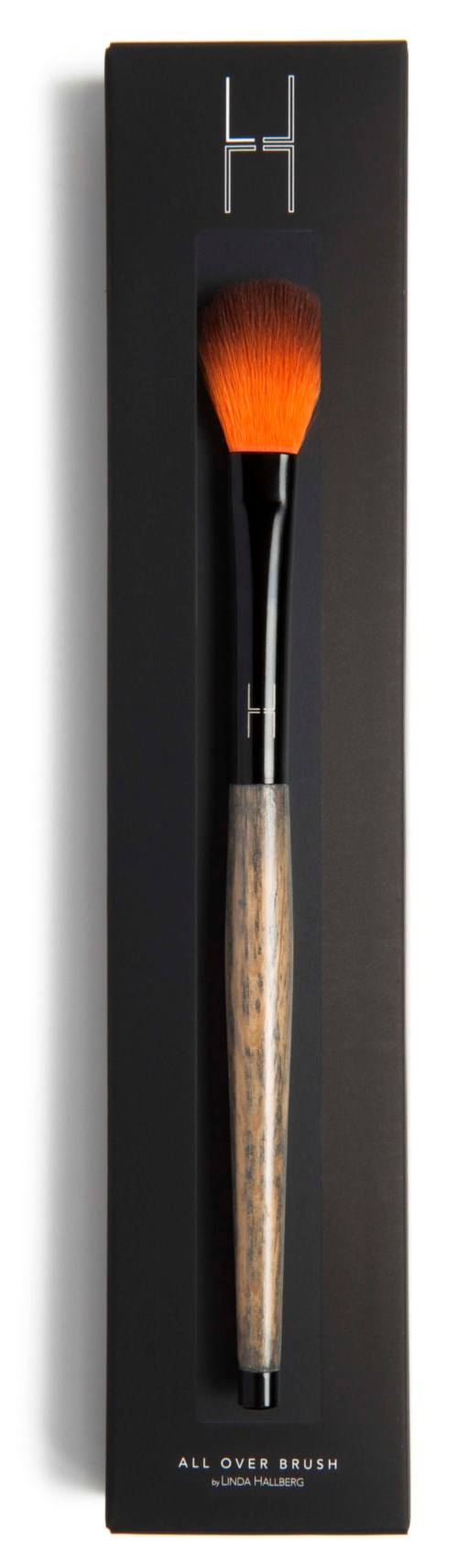 A makeup brush with a wooden handle and orange bristles in black packaging.