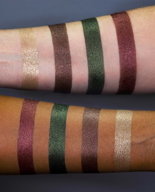 Proben verschiedener glitzernder Lidschattenfarben auf Armen, darunter Gold, Braun, Grün und Pink.