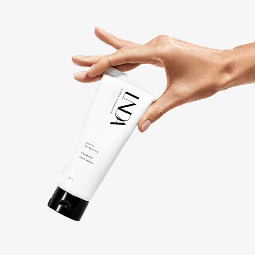 En hånd holder et hvitt rør merket med merkevaren LUX, muligens et hudpleie- eller kosmetikkprodukt.