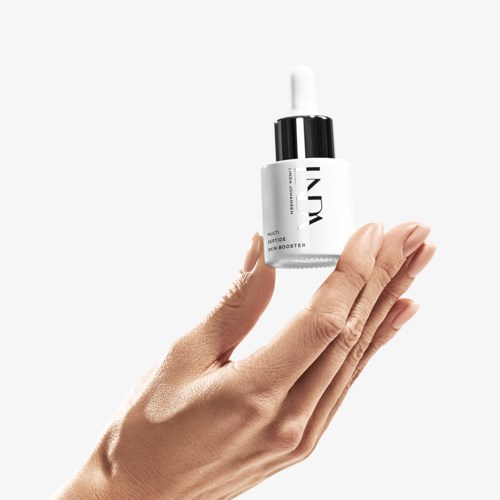 En hand håller en liten flaska med dropper, märkt "INDY". Flaskan verkar vara för hudvård eller skönhet. Två fingrar berör försiktigt flaskan.
