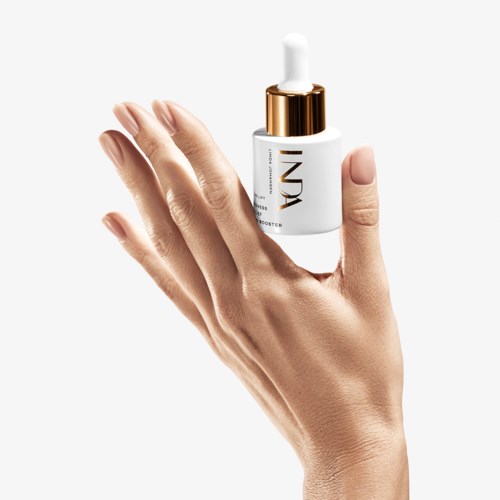 En hand håller en vit hudvårdsflaska med pump, gulddetaljer och texten 'INDI'.