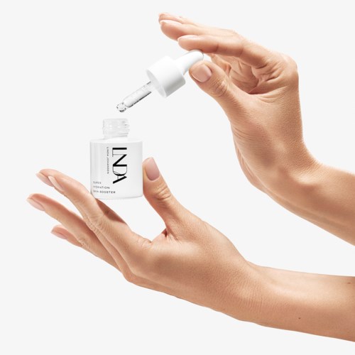 To hender holder en liten flaske med pipette og en dråpe som faller ut, noe som antyder et hudpleieprodukt eller serum.