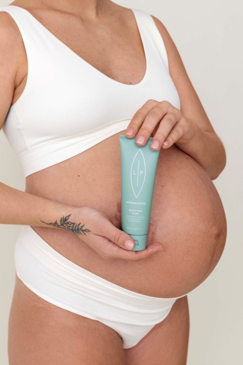Gravid kvinna som håller ett grönt hudvårdsrör på magen.