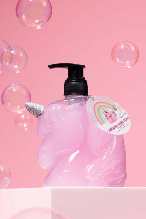 Roze eenhoornvormige fles met zwarte pomp, regenboog en eenhoornillustratie op een roze achtergrond met zwevende bellen.