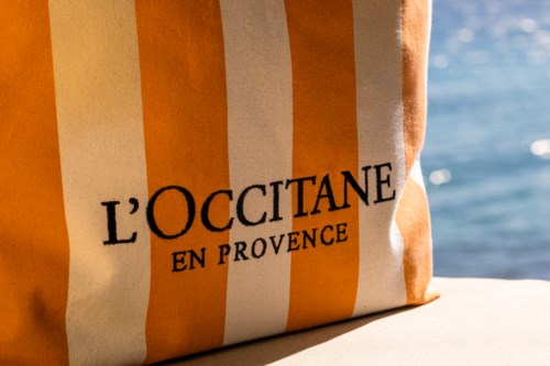 A striped bag with the words "L'OCCITANE EN PROVENCE" printed on it, near water.