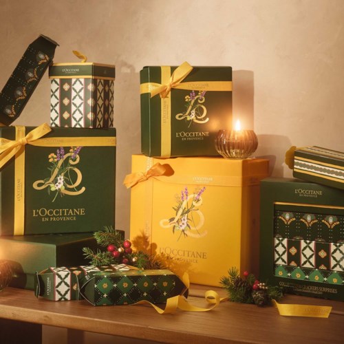Festliga presentaskar från L'Occitane med guldband, omgivna av juldekorationer och ljus.