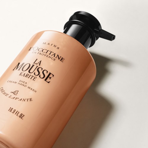 En ferskenfarget flaske med håndsåpe fra L'Occitane og svart pumpe. Tekst på flasken inkluderer produktnavn og detaljer.