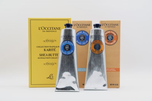 Two tubes of L'Occitane hand cream and mitt box with yellow and orange packaging in the background.