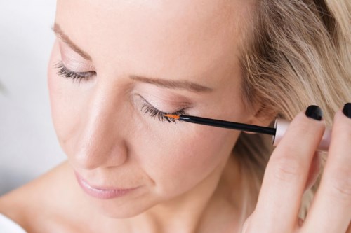 En kvinne påfører mascara på øyevippene sine, i et nært bilde av øyemakeup.