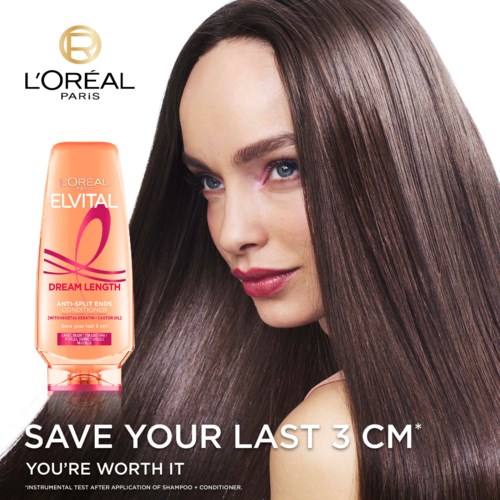 A woman with long, shiny brown hair smiles softly beside a bottle of L'Oreal Elvital Dream Length shampoo.