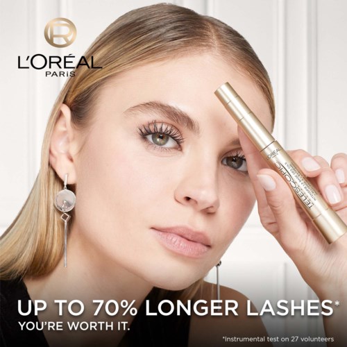 A woman with long eyelashes uses a gold L'Oreal brow serum, promoting longer lashes with a confident look.