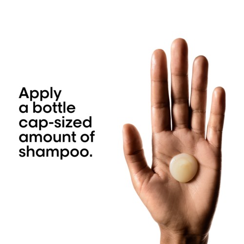 Hånd som holder en rund shampoo-kork med instruksjoner om å bruke en kapselstor mengde sjampo.