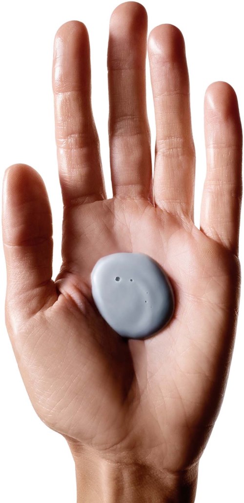 A hand with a gray circular object in the palm, fingers extended upward, against a light background.