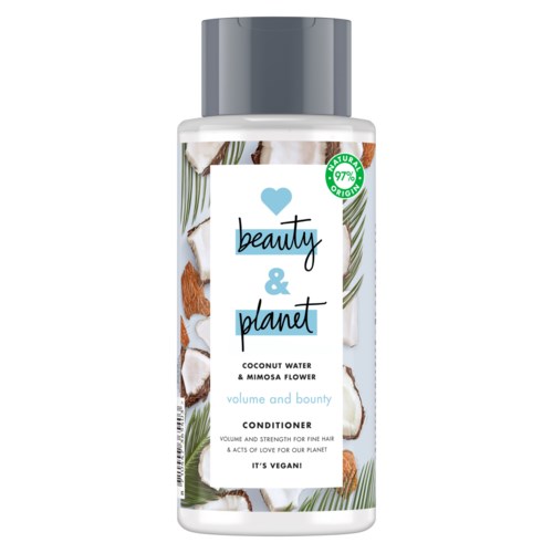 En hvit flaske med sølvhette merket "beauty & planet" kokosvann og mimosa blomst balsam. Bakgrunnen viser kokosbiter.