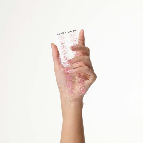 En hand håller ett transparent ark med rosa glitter och texten 'LOVEN LAYER'.