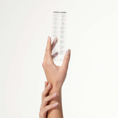 En hand håller ett litet transparent ark med små, detaljerade mönster och texten 'LOVE N LAYER' upptill.