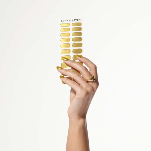 En hand med gyllene ringar håller en palett med gula makeupnyanser märkt "LOVE'N LAYER."