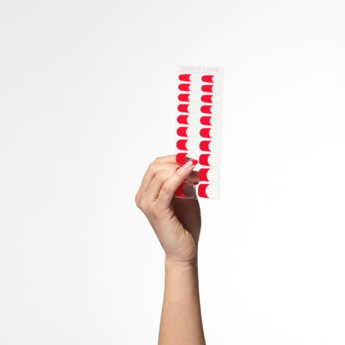 En hånd holder en stripe med røde og hvite halvsirkler og tekst øverst. Enkel hvit bakgrunn.
