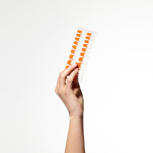 En hånd holder en stripe med oransje og hvite piller mot en hvit bakgrunn.