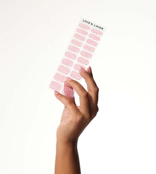 A hand holds a sheet of pink and white patterned stickers labeled 'LOVE N LAYER'.