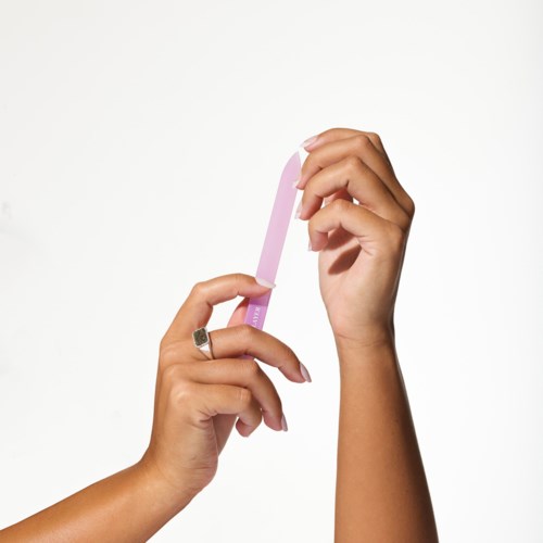 En hand håller en rosa och vit nagelfil mot en enkel bakgrund.