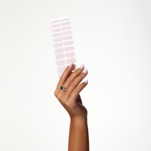 En hand håller rosa naglappapper med lila spetsar, mot en ljus bakgrund.