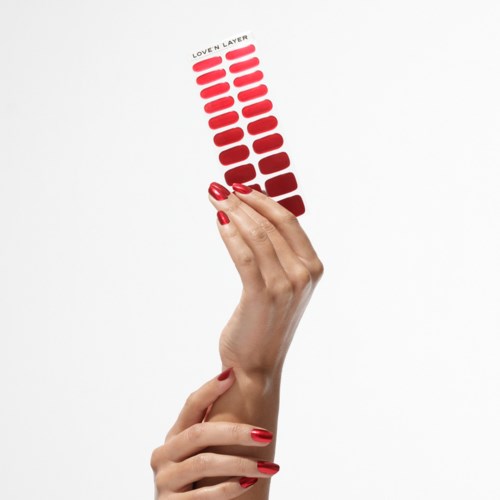 A hand with red nails holds a color palette labeled 'Love N Layer', featuring shades of red and pink on a white background.