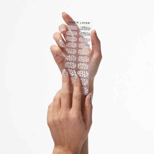 En person applicerar en genomskinlig nagelstrykare med vita virvlar på naglarna.