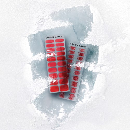 Zwei Blätter mit roten Leucht-Nagelsticker auf Schneefläche. Sie sind mit "Loven Layer" beschriftet.