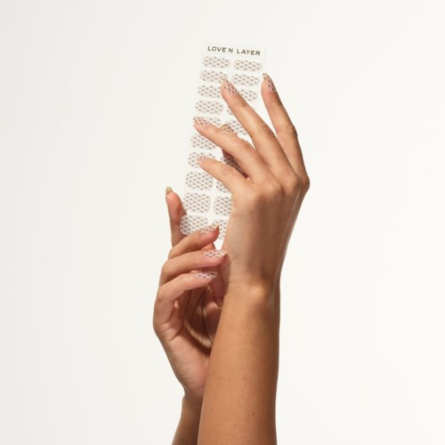 En hand håller i ett genomskinligt nagelklistermärkesark med etiketten "LOVEN LAYER" mot en vit bakgrund.