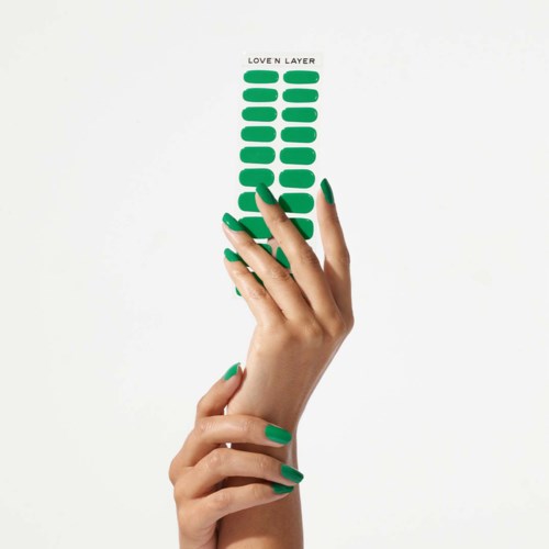 Green layered strips with the text "LOVE N LAYER" at the top, held by a hand with matching nails.