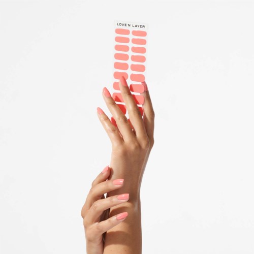 Eine Hand hält einen Streifen mit vielen pfirsichfarbenen Schichten, beschriftet "Love N Layer," vor weißem Hintergrund.