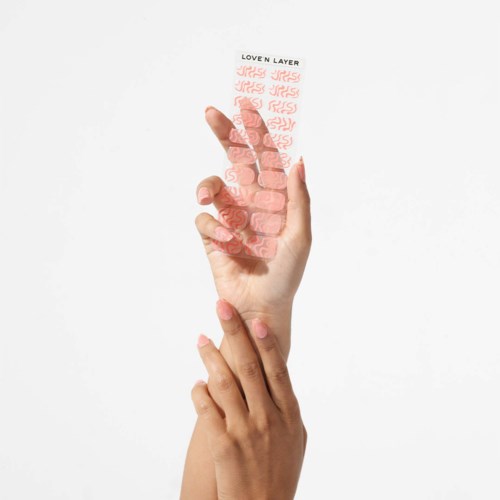 Een hand houdt een transparante nagelsticker met rode patronen en zwarte tekst, die 'LOVEN LAYER' zegt.