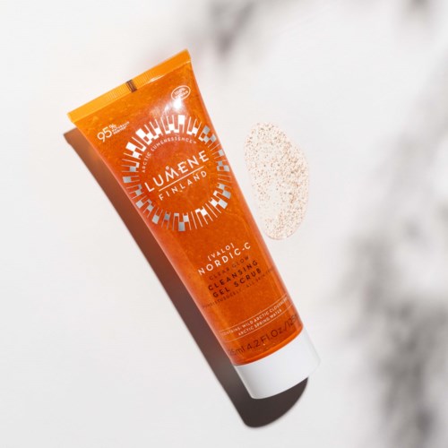 En oransje tube fra Lumene Nordic-C Rensende Gel Skrubb på en hvit overflate med en teksturert svamp i nærheten.
