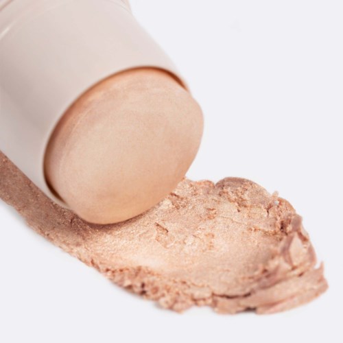 En beige tub med makeup-foundation med lite spilld produkt på en vit yta.