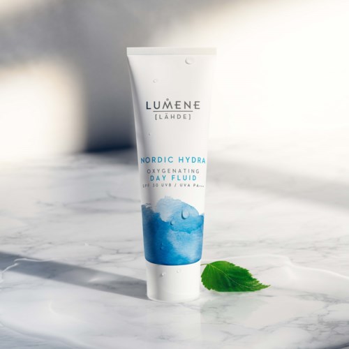 En vit tub från Lumene Nordic Hydra Day Fluid med vattenstänk och ett grönt löv bredvid.