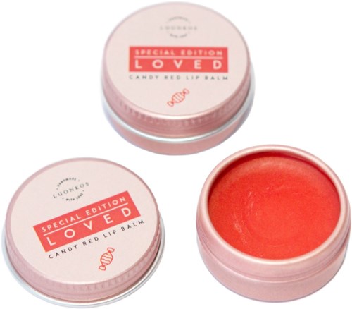 Pyöreä pinkki rasia, sisältää punaista huulivoidetta, merkitty 'Special Edition Loved' ja 'Candy Red Lip Balm.'
