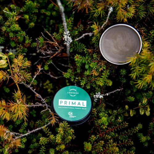 Een pot met bosbalsem met open deksel tussen groene planten en struiken.