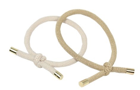 Två beige flätade snören med metalländar, knutna. De ser ut som dekorativa eller handgjorda tillbehör.