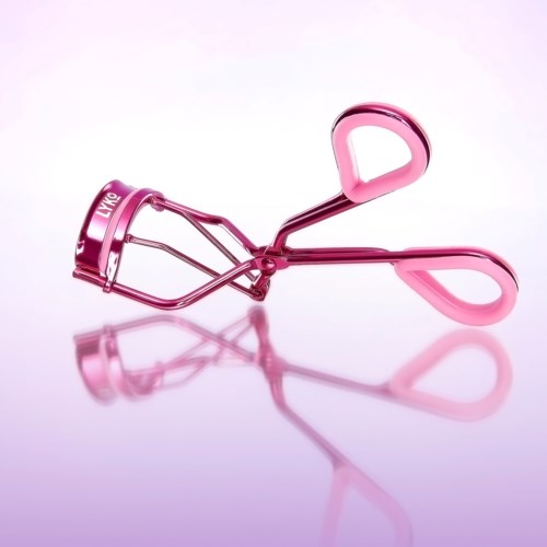 Ein pinkfarbener Wimpernzange mit zwei Griffen und einer gebogenen Metallklemme auf einer reflektierenden Oberfläche.