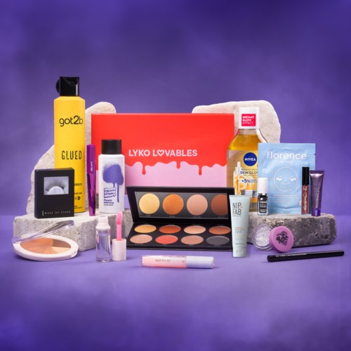 En samling skönhetsprodukter och makeupprodukter arrangerade på grå stenblock mot en lila bakgrund.