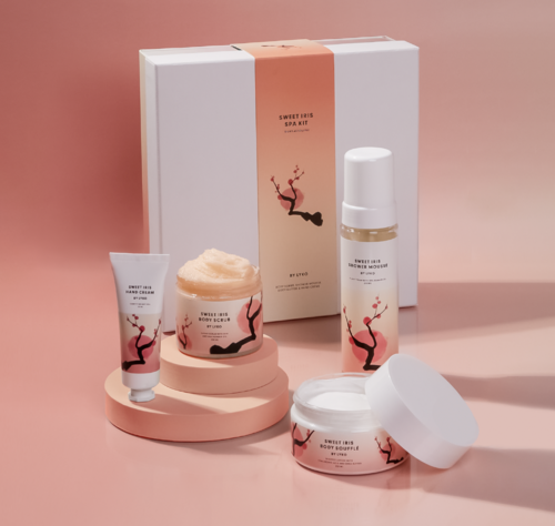 En hudpleiesett med eske, lotion, kroppsskrubb, håndkrem og kroppssoufflé, alle med matchende rosa og svart tre design.