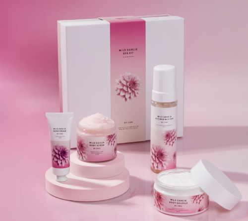 Ett set med wellnessprodukter i rosa och vitt med blommönster, inklusive lotions och krämer i burkar och flaskor.
