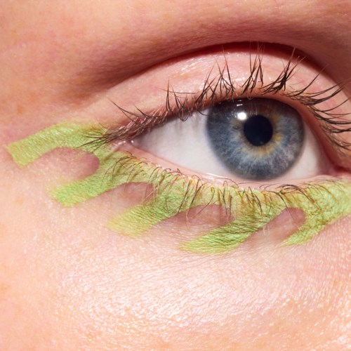 Close-up van een blauw oog met geelgroene oogschaduw onder het oog en op de oogleden.