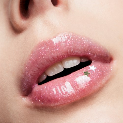 Close-up of lips with pink gloss and small star-shaped stickers. Some teeth are visible.